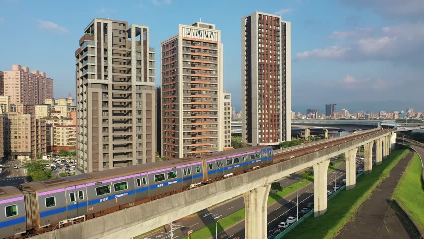 A metro train dashing on the elevated rail of Taoyuan Airport MRT on sunny day, with high rise residential towers booming in the nearby community, in Sanchong District, New Taipei City, Taiwan