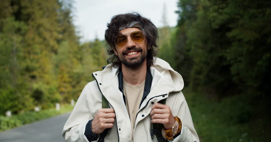 Portrait of a brunette tourist guy in big yellow glasses in a special uniform for tourists who poses and looks at the camera near the road against the backdrop of a mountain forest
