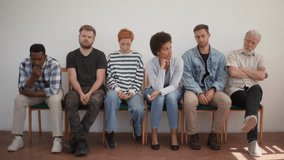 Tired diverse multiethnic and different ages candidates for vacancy sitting on chairs in queue feeling nervous bored waits job interview turn, on white isolated background. Shooting in slow motion. - Powered by Shutterstock - Get 15% off with code: PIKWIZARD15