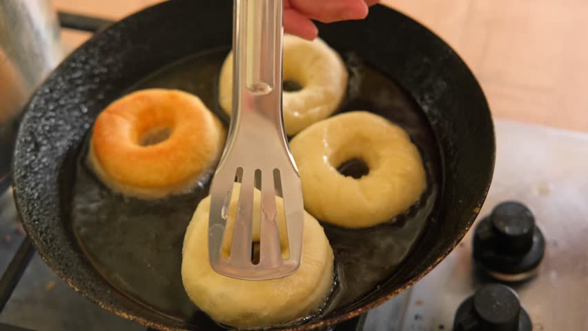 Frying process homemade and delicious donuts on fresh oil in a pan. Blue sugar topping on donuts in a home candy workshop. Pastry, sweet. Making dessert being deep fried. Preparation of donuts