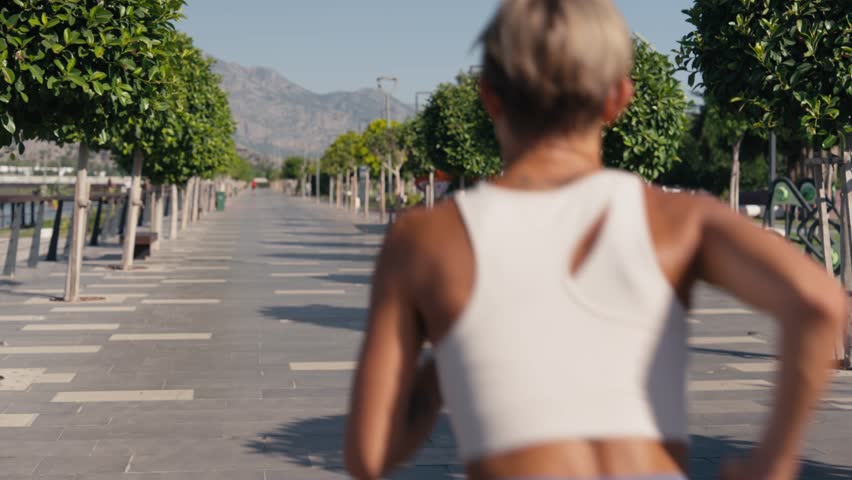 Young caucasian woman outdoors running and jogging at the city park on a sunny warm and bright day, surrounded by nature. High quality 4k footage