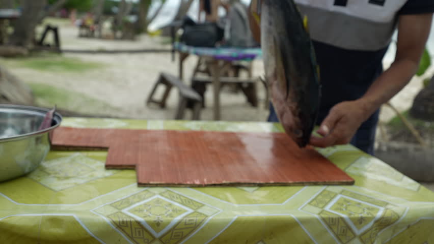Close-up of the hands of a person cutting freshly caught fish on a tropical beach in Southeast Asia
