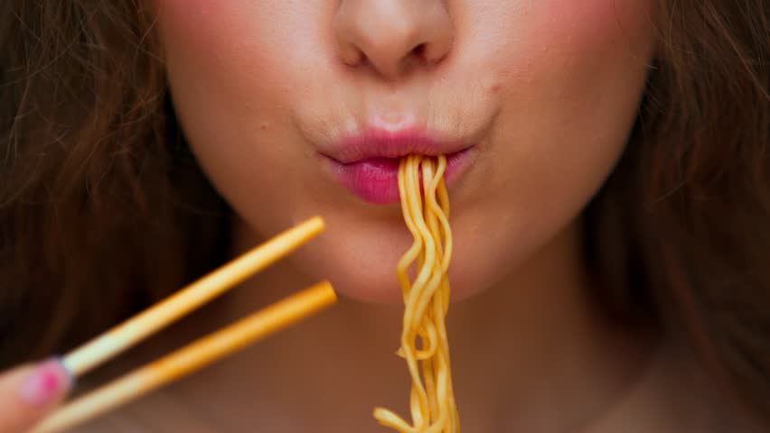 Portrait of Young Woman Eating Food on Camera. Crop Face of Real Person Consuming Instant Cup Noodles as Quick Dinner Meal. Alone Female Human with Chinese Chopsticks and Savory Korean Lunch in Mouth