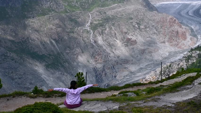 One girl is practicing yoga at mountain. Landscape of glacier, mountain and forest. Aletsch Glacier in Swiss Alps. Riederalp, Valais Canton, Switzerland. Travel destinations. Ice melting.