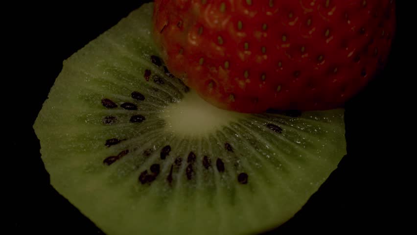 Kiwi fruit and strawberry rotating on black.