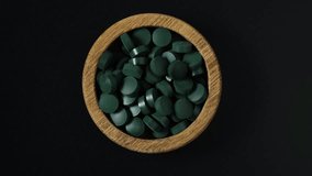 Green Spirulina pills in wooden bowl on dark background. 4K video, rotating. Pressed pills from seaweed extract are widely used in alternative medicine.