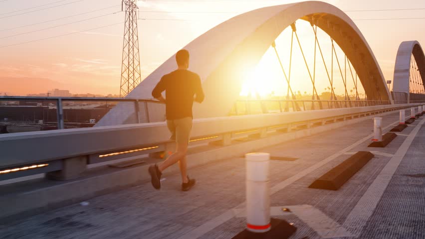 Athletic Man working out by jogging across the 6th Street Bridge over the LA River near downtown Los Angeles at dawn.