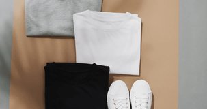 Video of flat lay of multi coloured t shirts with copy space on brown and grey background. Clothing, fabric, texture and materials concept.