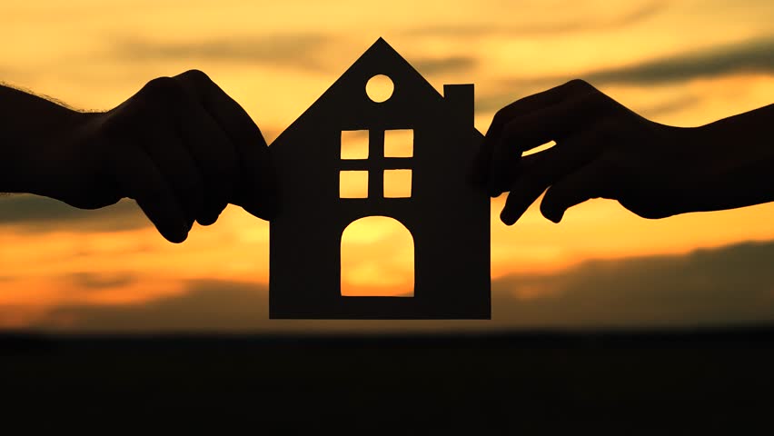 Familys hands are holding paper house at sunset, sun is shining through window. Symbol of house, happiness. Concept of building house for family. Dream to buy house. Home for children and parents Royalty-Free Stock Footage #1107099365