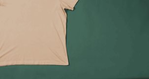 Video of yellow t shirt with tag and copy space on green background. Clothing, fabric, texture and materials concept.