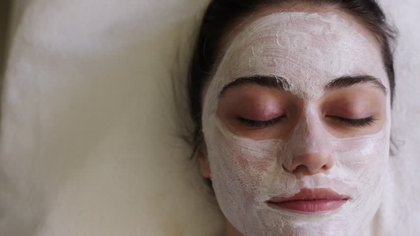 Close-up portrait of beautiful girl applying facial mask. Spa woman applying facial clay Mask. Beauty treatments.