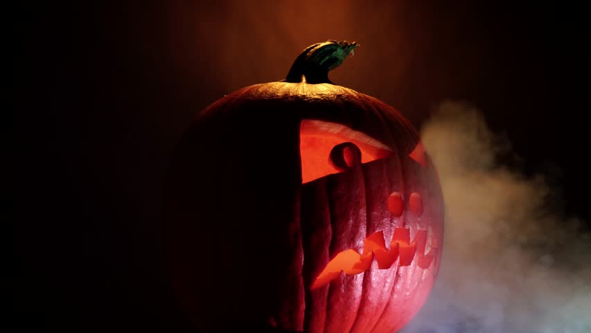 Happy Halloween scary glowing face of Halloween pumpkin, selective focus. Glowing scary Jack O Lantern spirit demon on black dark background. Traditional Halloween symbol. | Shutterstock HD Video #1107102557