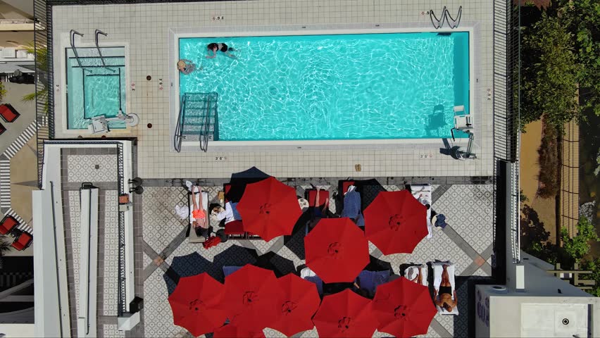 ascending overhead aerial footage of a people swimming and relaxing at a rooftop pool with a canal surrounded by lush green trees and grass at West Beach in Santa Barbara California USA Royalty-Free Stock Footage #1107102791