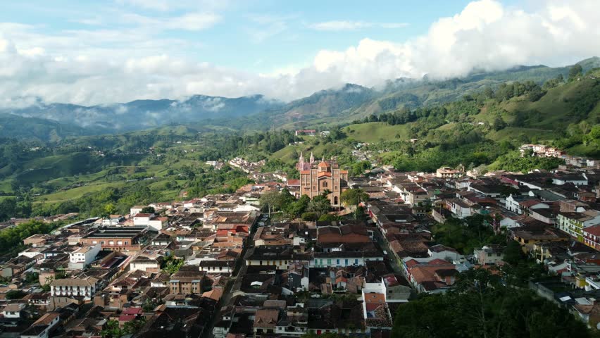 Aerial view of a small colonial town with big church towering from the main square, surrounded by lush green hills, Jericó, Antioqia, Colombia