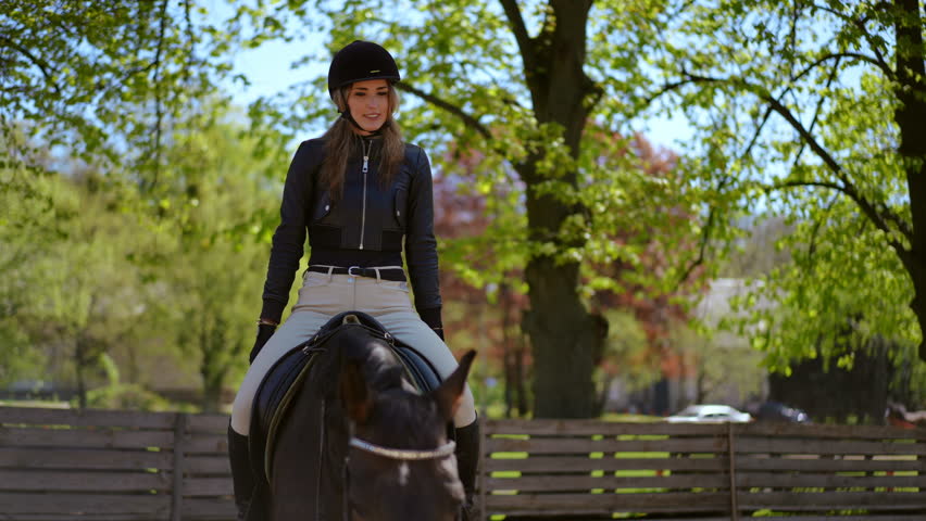Smiling professional equestrian training with purebred graceful horse in paddock on sunny day. Portrait of confident Caucasian slim beautiful woman stretching hands standing up sitting down in saddle Royalty-Free Stock Footage #1107112413