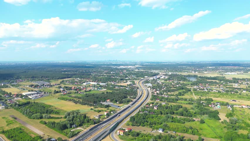 Aerial view of road in green meadows at sunset in summer. Top view from drone of rural road, forest. Beautiful landscape with roadway, sun rays, trees, hills, green grass, clouds. Poland