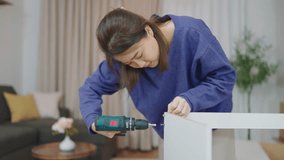 Young asian women using a drill for assembling new furniture by herself at home. Woman using a drill tightens screw on furniture assembling by herself. Assembling furniture concept - Powered by Shutterstock - Get 15% off with code: PIKWIZARD15