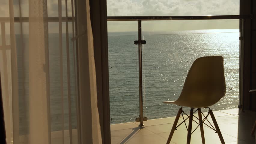 Beautiful Sea View Terrace Window at Sunset. Sea in the Rays of the Sun Sky and Clouds. Chair on Balcony with Relaxing Ocean View. Relax, Beauty, Vacation. Royalty-Free Stock Footage #1107117509