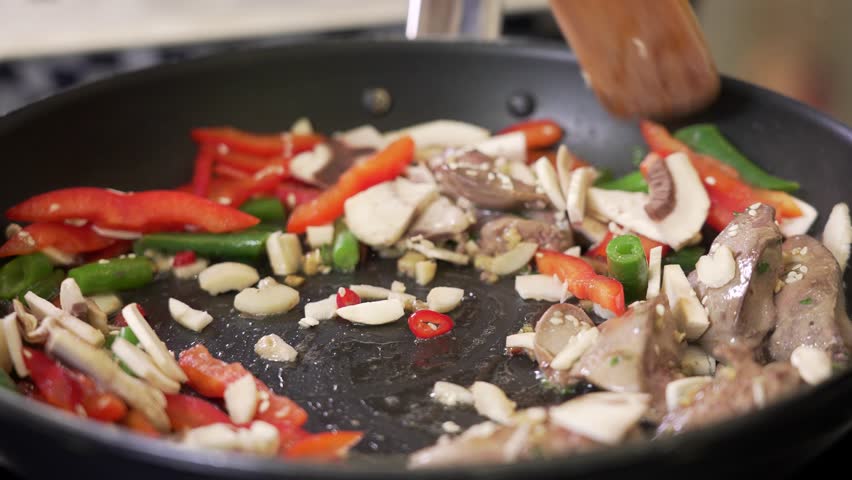 Frying chopped chicken liver with vegetables and mushrooms in a pan