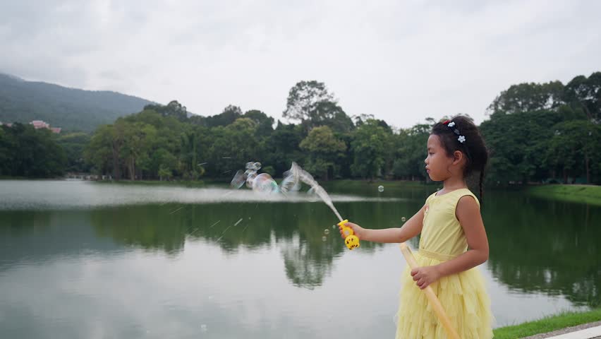 Little Asian girl alone at the lake playing soap bubble.