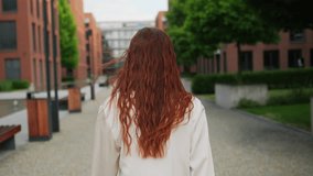A beautiful red haired woman walking in the street, turning around and looking into the camera. 