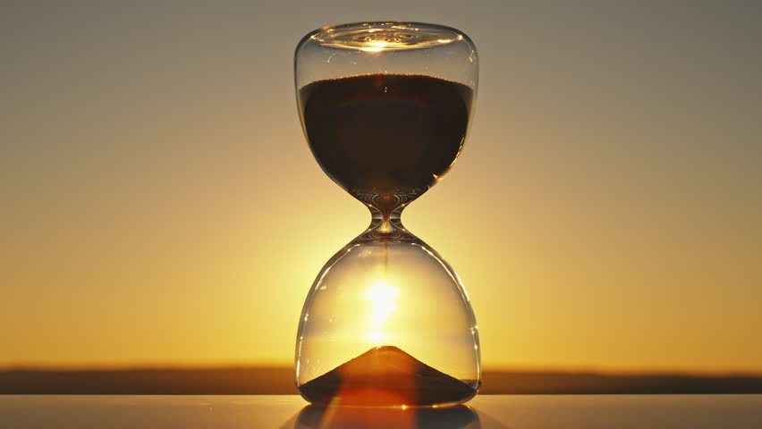 Silhouette hourglass time concept on blurred background of golden sun disk sky in sunset rays in summer closeup evening. Golden sand pours quickly. Time concept sand. Relax Royalty-Free Stock Footage #1107124545