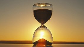 Silhouette hourglass time concept on blurred background of golden sun disk sky in sunset rays in summer closeup evening. Golden sand pours quickly. Time concept sand. Relax - Powered by Shutterstock - Get 15% off with code: PIKWIZARD15