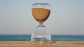 Timelapse hourglass concept on blurred background of waves of blue sea blue sky in sunset rays in summer closeup. Golden sand pours quickly. Time concept sand. Relax. Freedom - Powered by Shutterstock - Get 15% off with code: PIKWIZARD15
