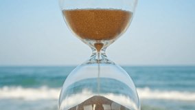 Time concept Hourglass concept  sand on blurred background of waves of blue sea blue sky in sunset rays in summer close up slow motion. Golden sand pours quickly. Relax - Powered by Shutterstock - Get 15% off with code: PIKWIZARD15
