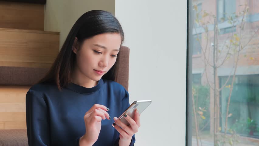 Young woman using her mobile phone and then smiling at the camera, Beijing, China