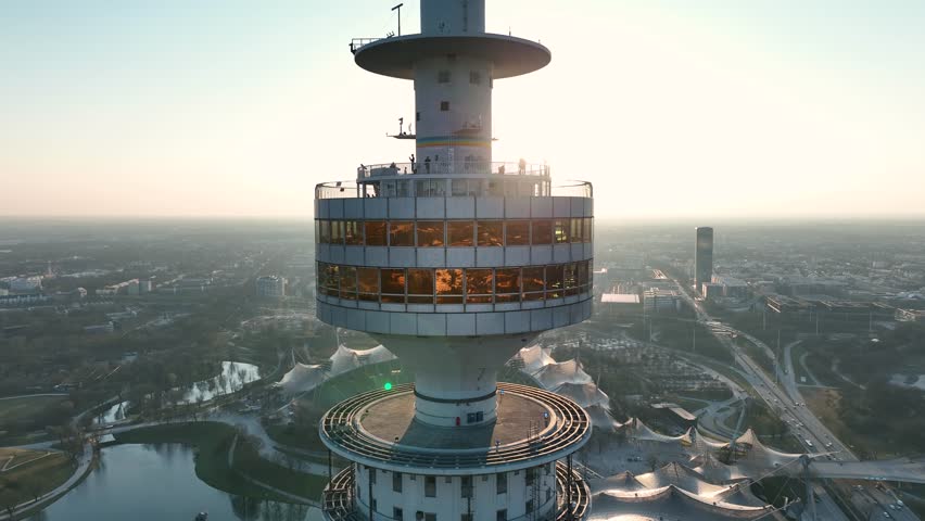 The drone is flying close around the olimpic tower during sunset with people on the tower and the olimpia park in the background in Munich Germany Aerial Drone Footage 4k Royalty-Free Stock Footage #1107126963