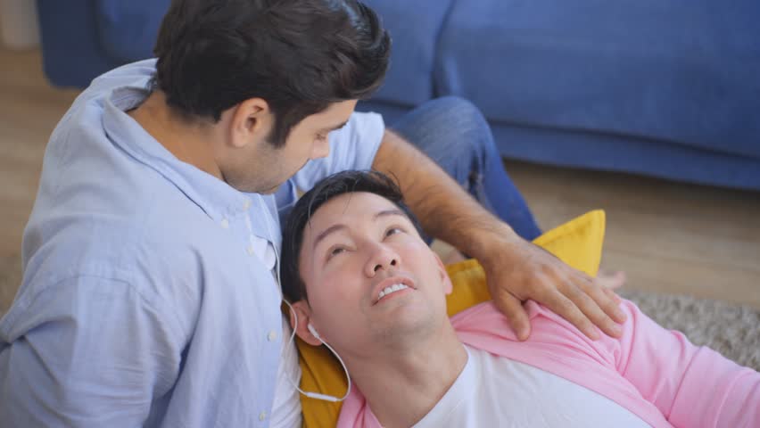 Caucasian handsome gay kissing each other while lying down in living room. Atractive romantic loving LGBTQ man couple feeling happy and relax, enjoy spending leisure free time together in house.