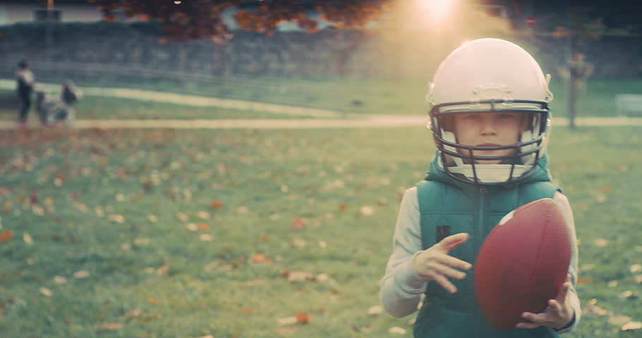 Family fun outdoors, Cheerful happy child in helmet playing American football outdoors in sunny day at public park. Family sports weekend. 4K video.
