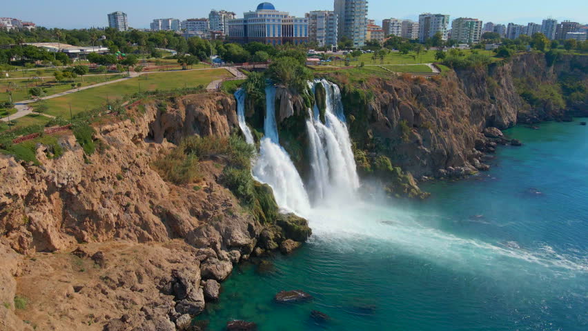 Slowmotion aerial video of the Lower Duden Waterfall in the city of Antalya. The drone moves above the Duden park revealing the surrounding park and buildings.