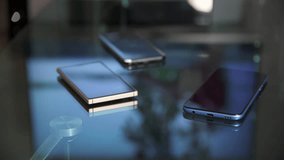 4K video of mobile phones on glass table with reflection of TV