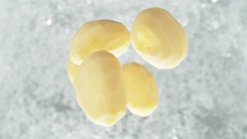 Peeled Potatoes Falling into Pot of Boiling Water Making a Splash in Slow Motion - Table Top View