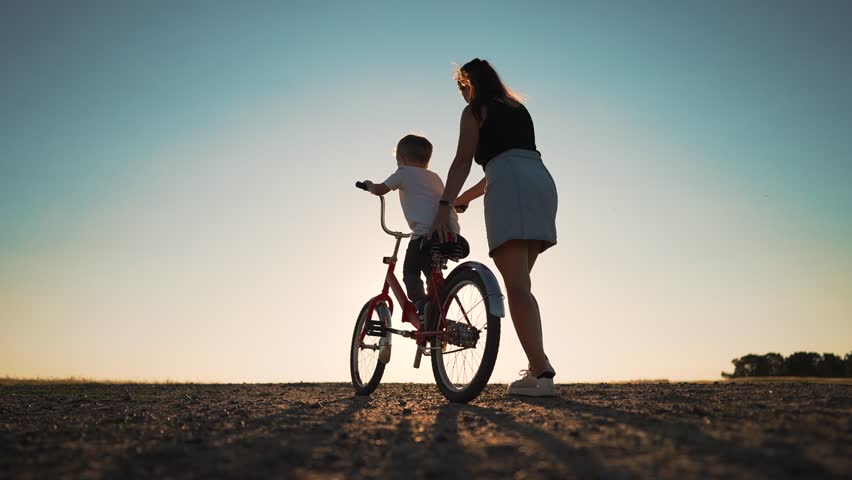 Happy family. Mom teaches her son to ride bike in park. My son is riding a bike for the first time. The child dreams of traveling by bike. The boy is learning to ride a bike. Mom helping hand to son. Royalty-Free Stock Footage #1107139629