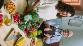 Senior family couple recording video recipe for food blog in the kitchen, telling about cheese and fresh vegetables, showing chefs kiss gesture on camera. Vertical clip