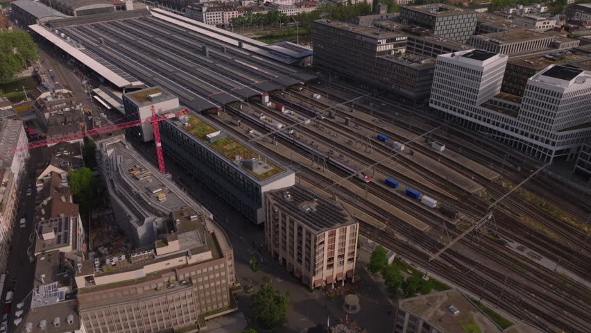 High angle view of town development. Fly above Hauptbahnhof with commuter trains leaving station. Tilt up reveal cityscape and lake in background. Zurich, Switzerland