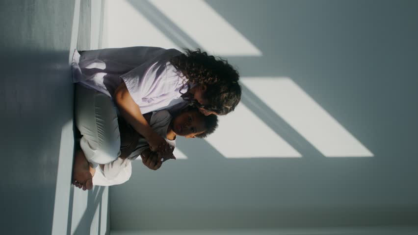 Mom and daughter of African-American appearance hugging sitting on the floor in a white room