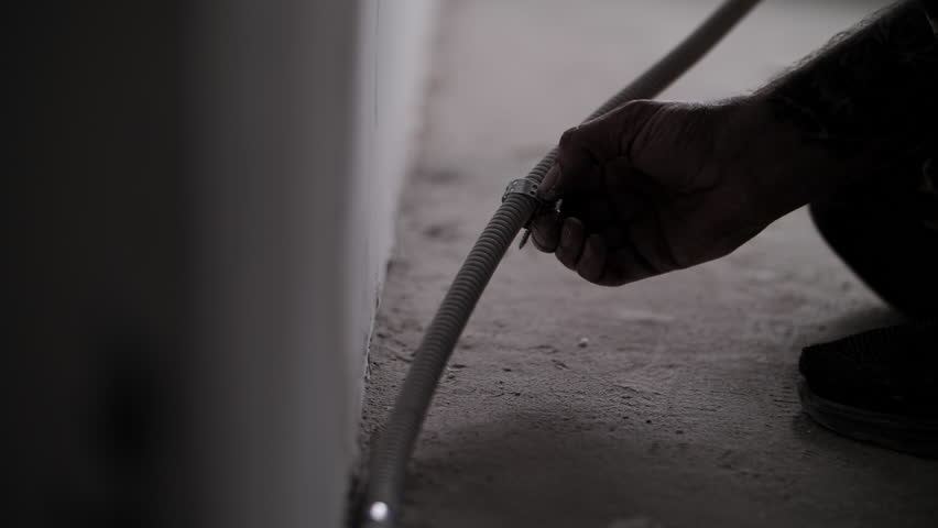 An electrician installs a corrugation with a wire in the apartment