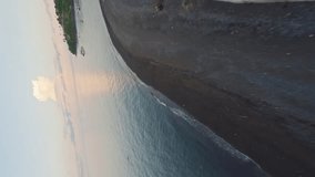 Vertical video. FPV sport drone moving over rippling sea with floating yachts near mountain covered greenery in calm summer evening at resort. Aerial low dynamic sunset island blue ocean water view 4k