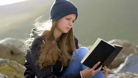 Young woman reading a book while sitting at a rocky beach - slow motion clip 