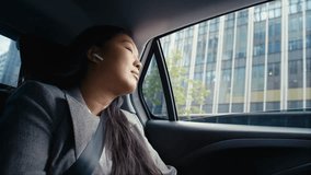 Business Chinese woman driving in a taxi and using earphones. Shot with RED helium camera in 8K. 