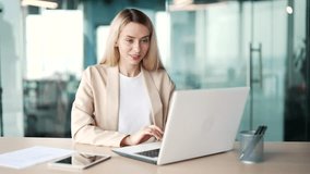 A young businesswoman typing on a laptop while sitting at a desk at a workplace in a modern office. Blonde female employee working on a project on the computer, texting a client or chatting online - Powered by Shutterstock - Get 15% off with code: PIKWIZARD15