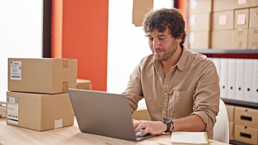Young hispanic man ecommerce business worker typing on computer with winner gesture at office