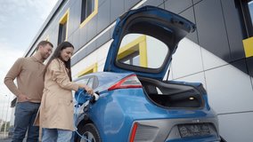 Happy young couple smiling outdoor at EV charging station. Joyful woman install charger plug from charging station to electric car. Zero emission car - Powered by Shutterstock - Get 15% off with code: PIKWIZARD15
