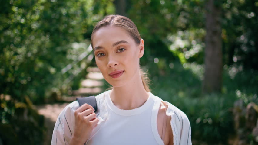 Active woman strolling park looking around on beautiful fresh greenery close up. Attractive serene lady walking green forest enjoying sunlight. Happy tranquil girl traveler relaxing on nature alone.