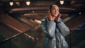 Carefree relaxed girl enjoy favorite song in headphones standing alone at urban backdrop. Attractive young woman closing eyes listening music by headset. Happy brunette feeling joy hearing sounds. - Powered by Shutterstock - Get 15% off with code: PIKWIZARD15