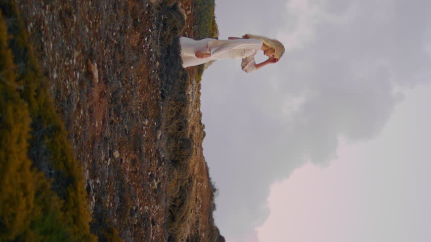 Serene model going nature cloudy sky background. Seductive girl wearing dress walking sunset grassy hill. Young happy lady looking distance relaxing green valley. Blonde woman spending evening alone